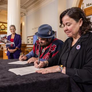 Two people sign papers while a third in the background looks on