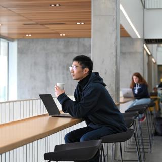 Jiayi Li sitting at a table with a cup of coffee looking out the window