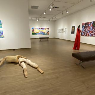 Interior of the View Gallery with paintings hung on the wall and a wooden human body art piece on the floor.