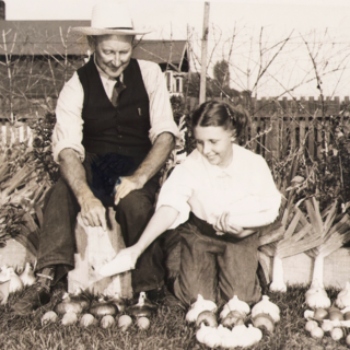 A man and a woman kneel behind produce laid out on grass