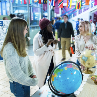 Three woman standing and chatting in front of a table on which sits two globes.