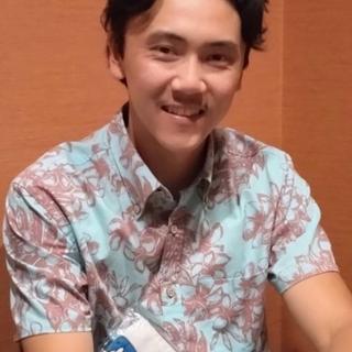 Kenji Boyko smiling. He wears a blue shirt decorated with maroon flowers.