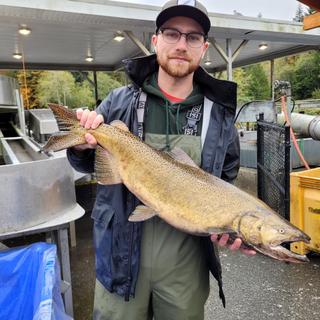 A man wearing hip waders and waterproof jacket holds a salmon