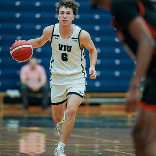 Ryan Bastian wearing a Mariners uniform running with the basketball during a game in a gym.