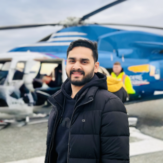 Saurya Mishra standing outside in front of a Heli-Jet helicopter and looking at the camera.