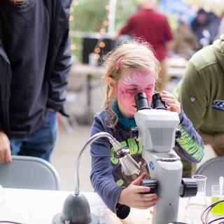 A young girl looking through a microscope during an exhibit at VIU Fest.