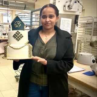 Zuhur Debasay holding a cake she made at VIU and smiling at the camera.