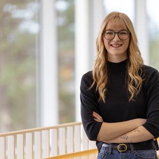 A student stands in front of a railing with her arms crossed