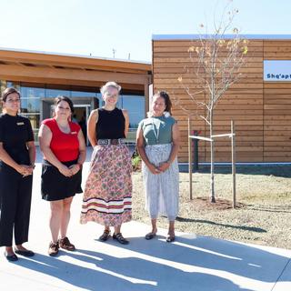 Four people stand in front of Shq'apthut: A Gathering Place