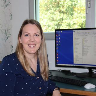 VIU Psychology Professor Becky Earhart sitting at her desk in front of a computer screen and smiling at the camera.