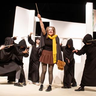 An actor hold their wand in the air as they fight off five dementors played by their casemates.