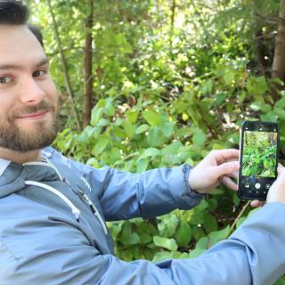 Jacob Frankel holds up his phone to a sala bush. The green leaves appear on his phone screen.