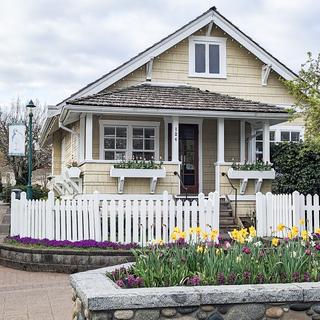 A building painted yellow with a white picket fence around it and a flower box with tulips out front.