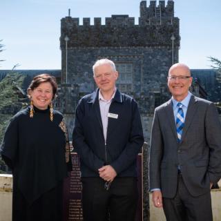 Three people standing in front of Royal Roads University