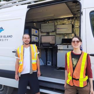 Trevor Michalchuk and Lily Eggert, wearing high visibility vests, while standing in front of the Mass Specmobile.