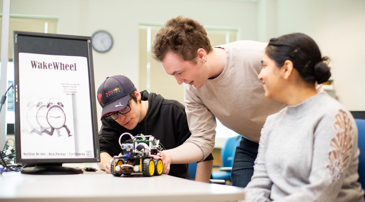 three students look at a robotic car on a table