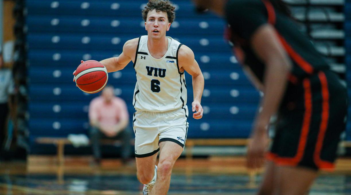 Ryan Bastian wearing a Mariners uniform running with the basketball during a game in a gym.