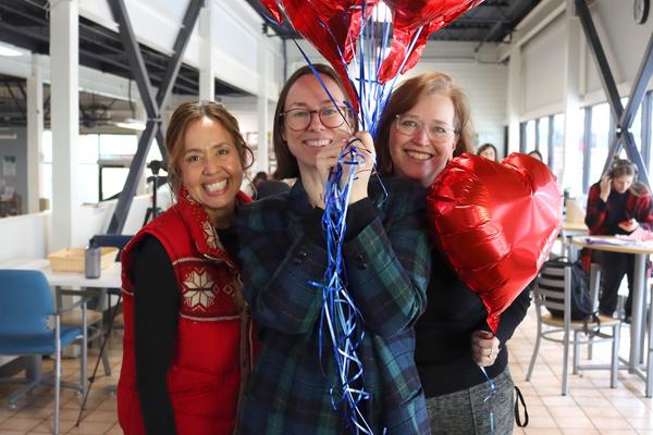 Three women stand with red balloons in support of Giving Tuesday