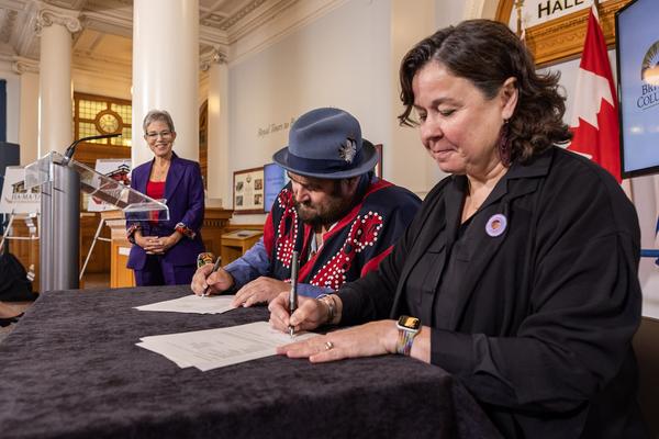 Two people sign papers while a third in the background looks on