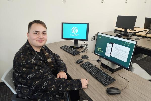 Andrew Szilagyi sitting in front of a computer and smiling at the camera. ChatGPT is on the screen in the background.