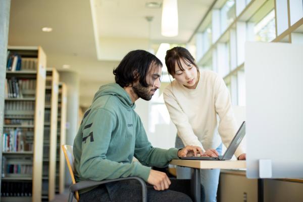 Two people look at a laptop screen in the library