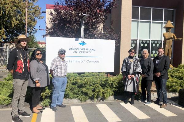 People standing in front of a sign announcing the renaming of a campus.