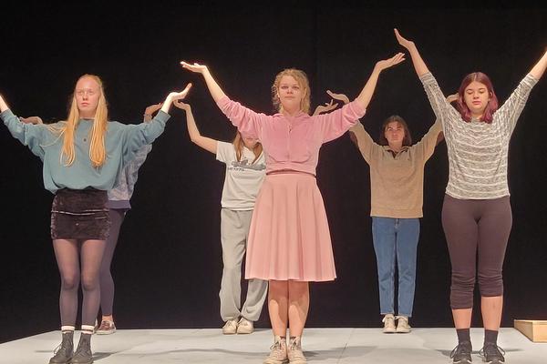 Six actors stand in two lines holding their arms up over their heads while rehearsing a scene at Malaspina Theatre.