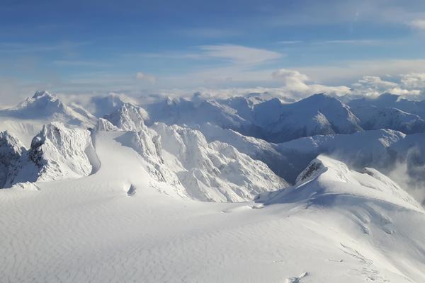 Mountain peaks covered in snow with a cloudy blue sky overhead.