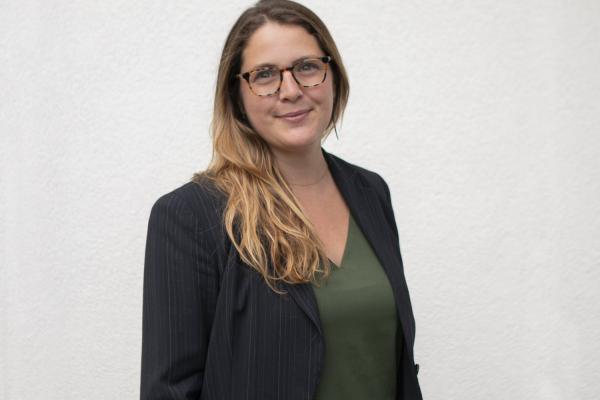 Dr. Amanda Wager, wearing a green shirt and black blazer, stands in front of a white wall.