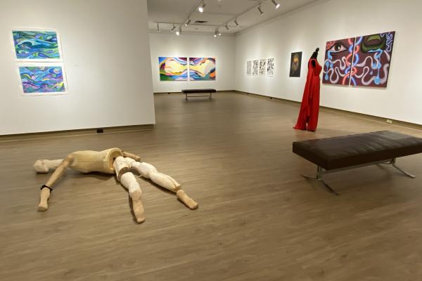 Interior of the View Gallery with paintings hung on the wall and a wooden human body art piece on the floor.