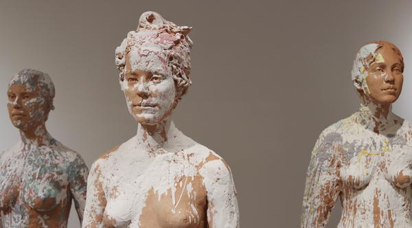 Three sculptures of a person splashed with white paint.