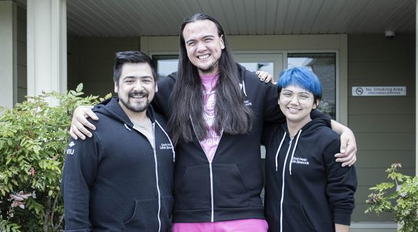 Three people standing in front of a VIU residence building