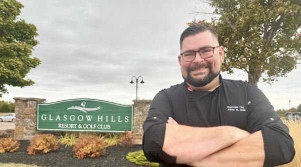 Aaron Smith standing by the Glasgow Hills resort sign with his arms folded and smiling at the camera.
