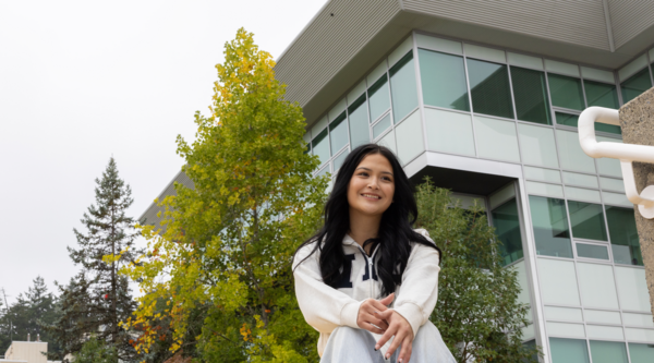 Marissa Tom-Charlie sitting on steps outside on a cloudy day, smiling and looking off into the distance