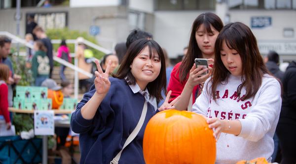 three students carve a pumpkin together