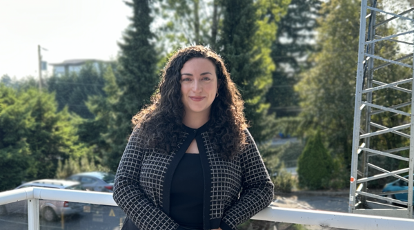 Caitlin Lundgren standing outside leaning on a railing on a sunny day and looking at the camera.