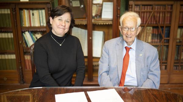 Deborah Saucier and Stephen Jarislowsky signing documents seated at a table