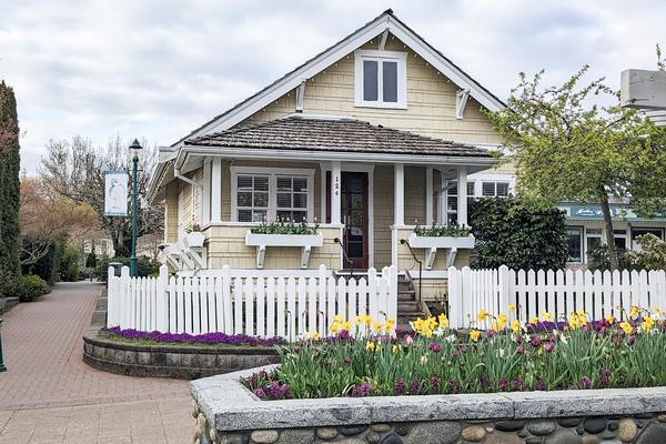 A building painted yellow with a white picket fence around it and a flower box with tulips out front.