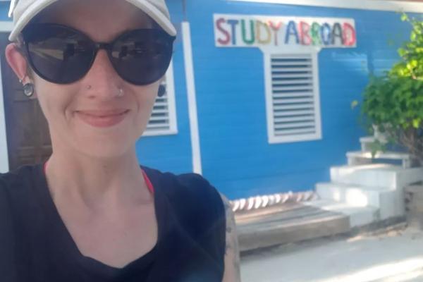 Melanie stands in front of the Tobacco Caye sign, which reads Study Abroad underneath it