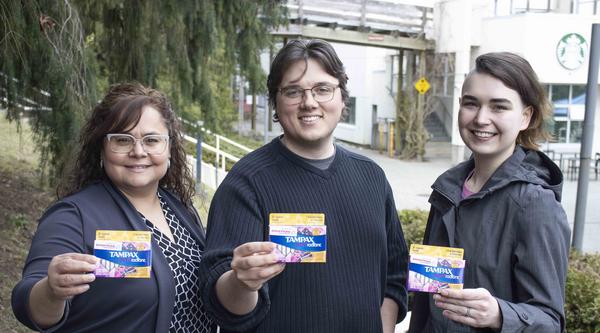 Three people hold up tampon boxes