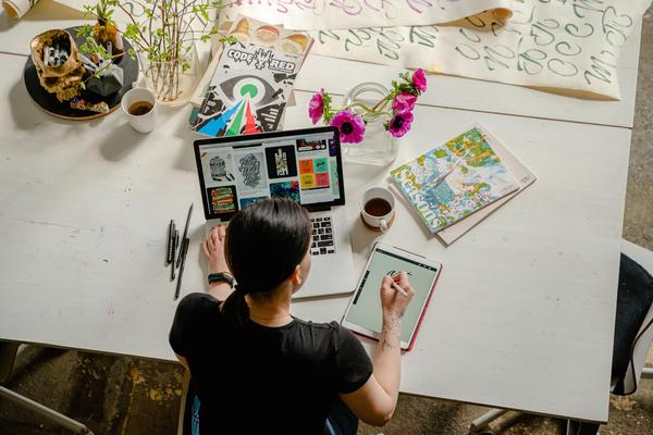 above view of a person with a laptop in front of them, notepad next to them and crafting materials around them