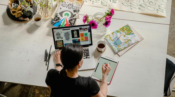 above view of a person with a laptop in front of them, notepad next to them and crafting materials around them
