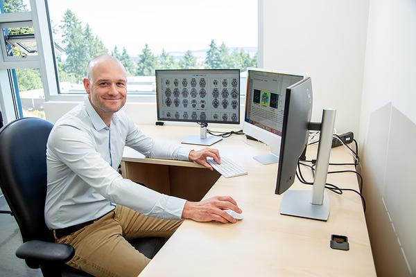 Sandy sits at his desk with images of brains open on one screen