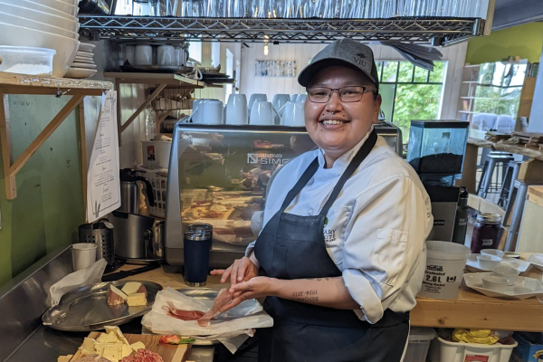 VIU Culinary Arts student Darlene Charlie making a sandwich in the Birch Tree cafe kitchen and smiling at the camera