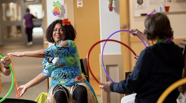 Telma Dos Santos sitting in a chair in front of a group of seniors who are all playing with a Hua hoop in their hands