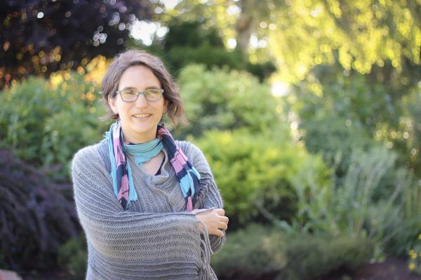 Sharon Karsten standing and smiling with her arms crossed in front of a blurred background of greenery