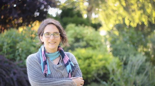 Sharon Karsten standing and smiling with her arms crossed in front of a blurred background of greenery