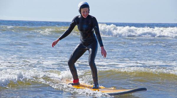 A woman wearing a wetsuit stands up on a surfboard