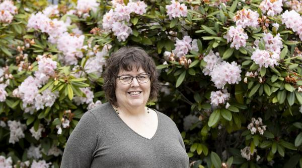 Terri Doughty, a VIU English Professor, smiles while standing in front of a rhododendron plant.