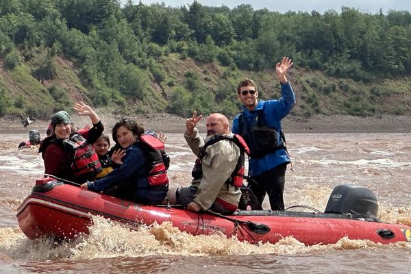 Lucas Gamp in a raft on a river with clients waving at the camera